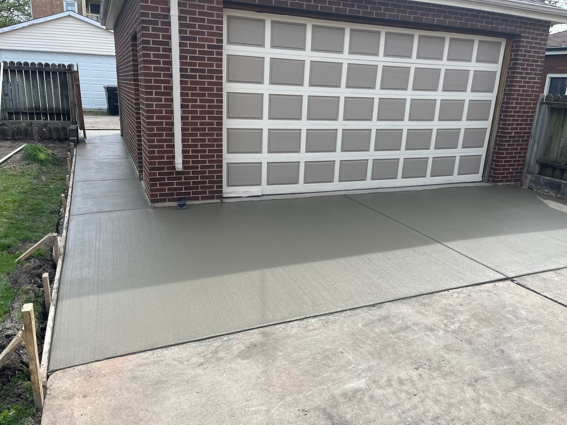 Freshly poured concrete driveway leading to a brick garage with a patterned door.