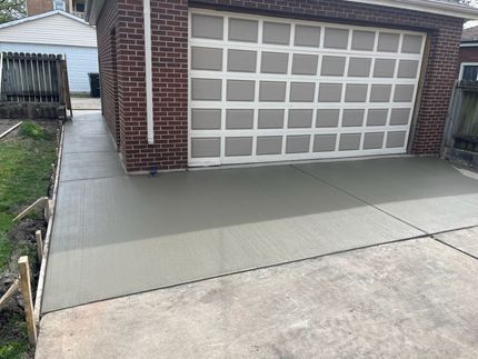 Freshly poured concrete driveway leading to a brick garage with a patterned door. Freshly poured concrete driveway leading to a brick garage with a patterned door.
