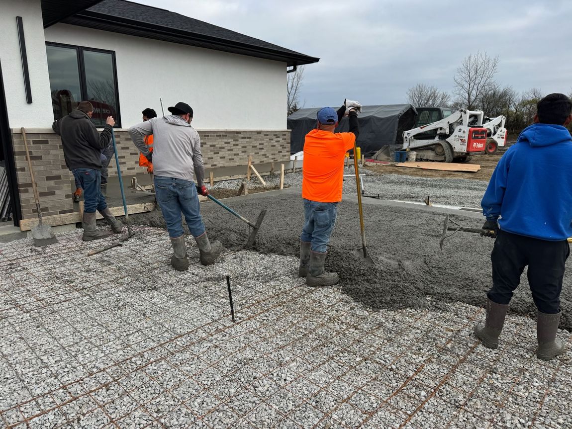 Construction workers leveling concrete on a prepared gravel base near a house. Construction workers leveling concrete on a prepared gravel base near a house.