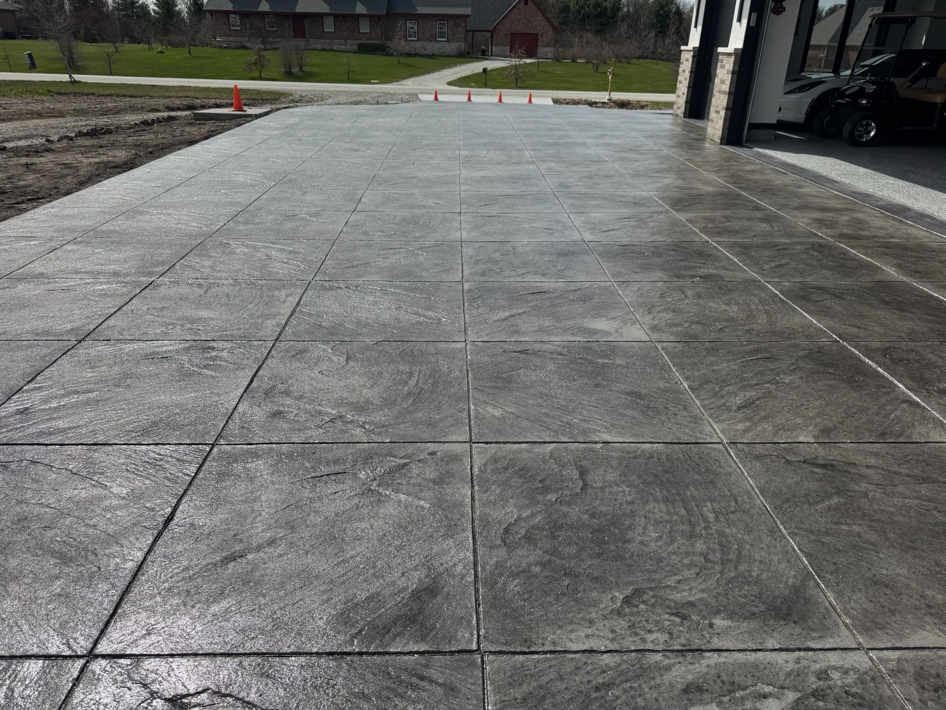 Gray concrete driveway with a tiled texture, leading towards a garage.