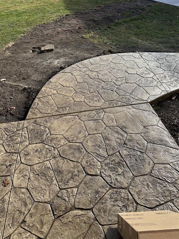Stamped concrete walkway with a stone pattern, in front of a green lawn and dirt.