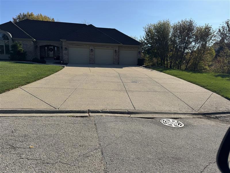Concrete driveway leading to a three-car garage. Green grass surrounds the driveway. Bright, sunny day.