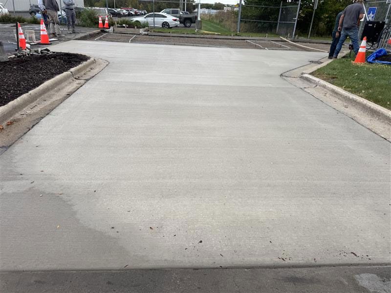 New concrete in a parking area, flanked by curbs and landscaping. Workers are present.