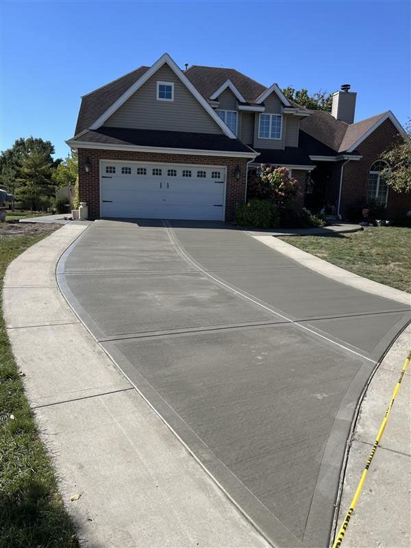 Newly poured concrete driveway in front of a two-story house with a brick facade and white garage door.