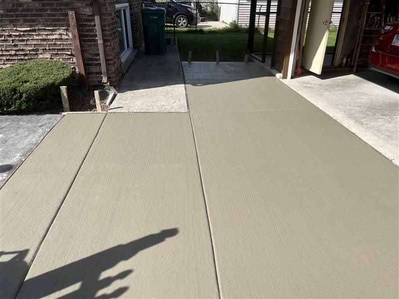 Newly poured concrete walkway and driveway next to a brick building and garage.