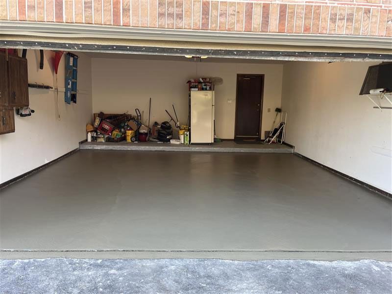 Garage interior with newly coated, gray floor. Tools and storage visible on walls, closed door in the back.