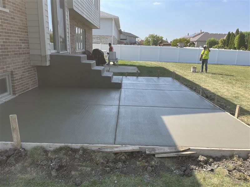 Newly poured concrete patio next to a house with steps. A worker stands nearby.