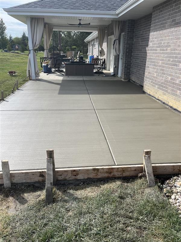 Newly poured concrete patio next to a brick house with a covered seating area.
