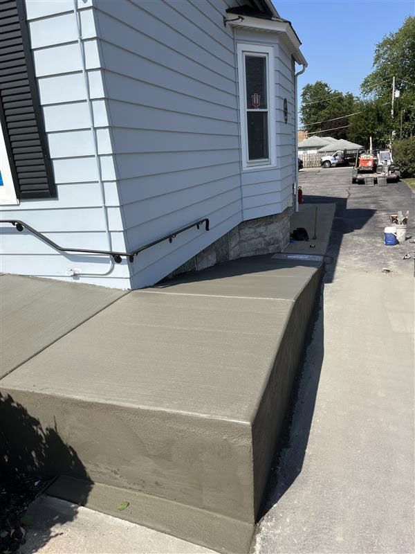 New concrete steps and walkway leading up to a light blue house with a black shutter and a small window.
