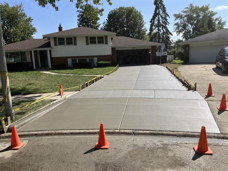 Newly poured concrete driveway with orange safety cones in front of a house.