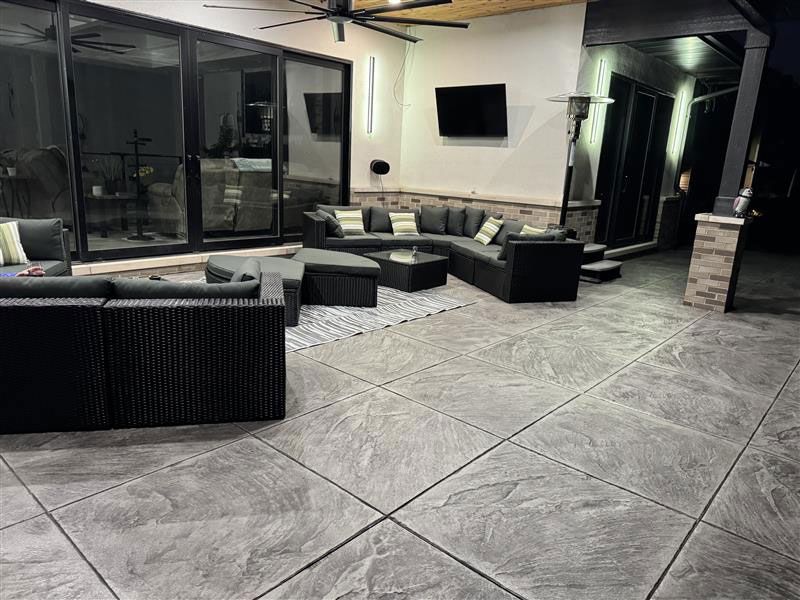 Patio with dark gray sectional seating, TV, and stamped concrete flooring.