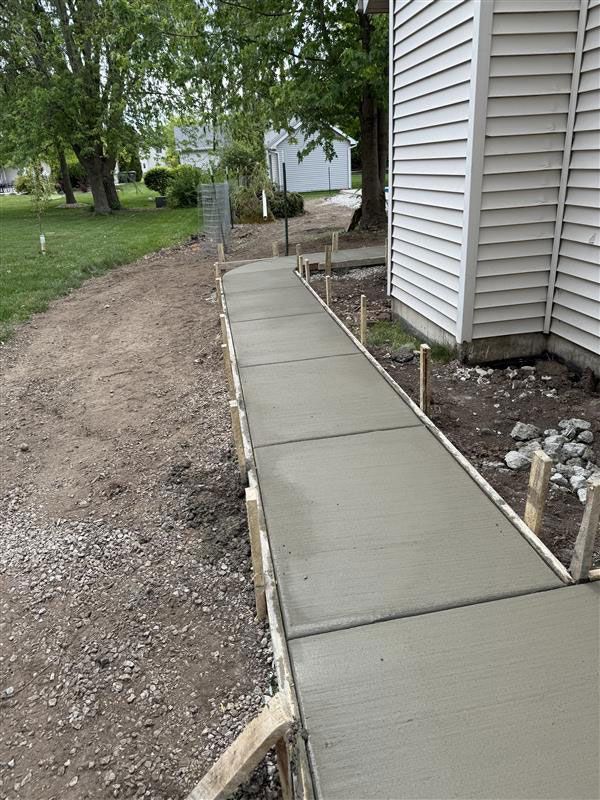 Newly poured concrete sidewalk next to a house with wooden forms still in place.