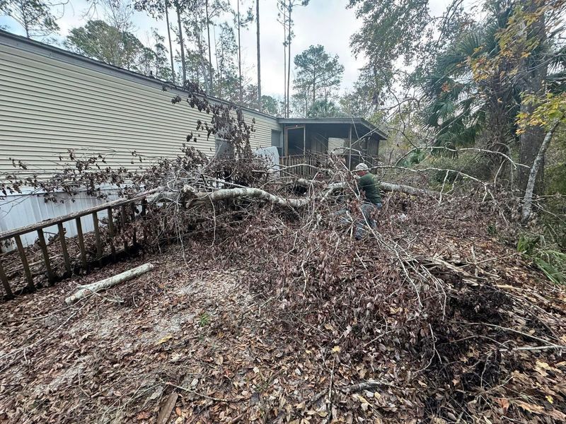 A home with debris and a person clearing tree branches.