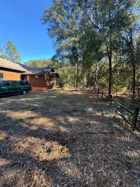 Yard with brown-sided house, trees, and a green vehicle. 