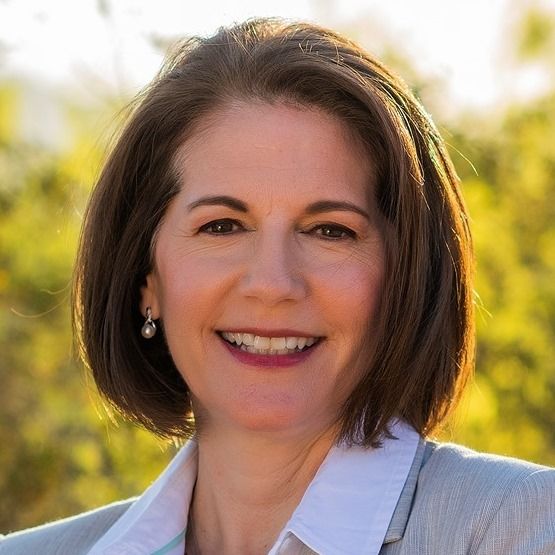 A woman in a suit and white shirt is smiling for the camera.