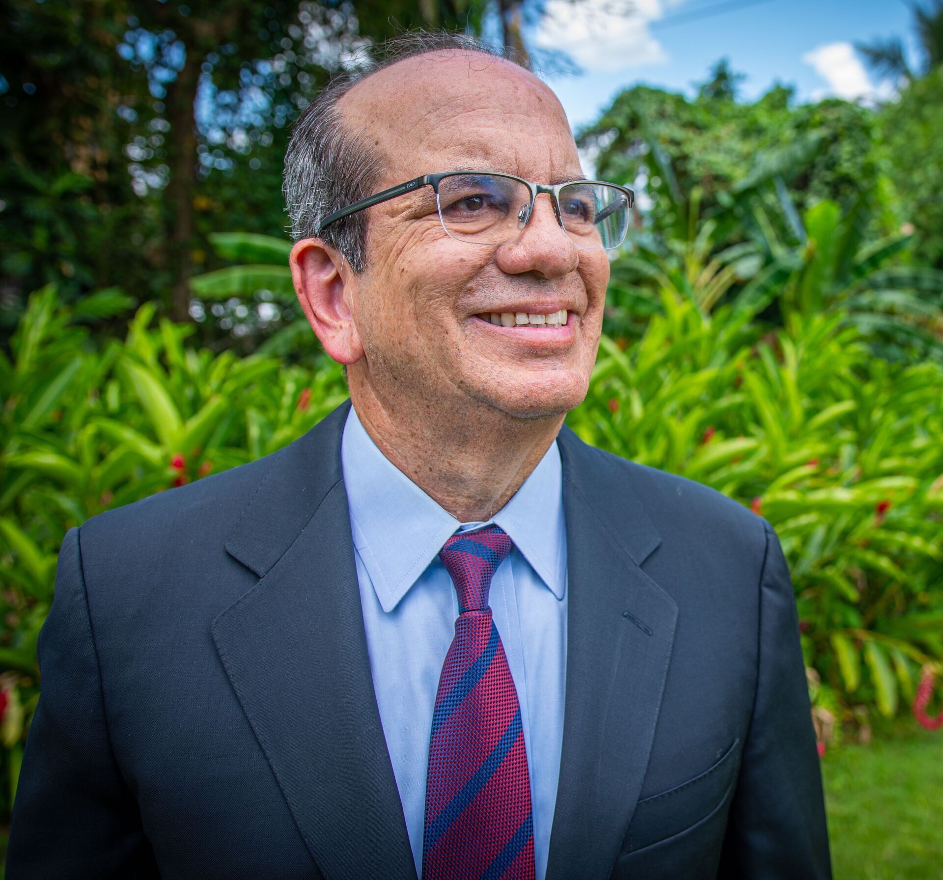 A man in a suit and tie is smiling and wearing glasses.