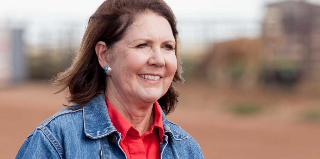 A woman wearing a denim jacket and a red shirt is smiling.