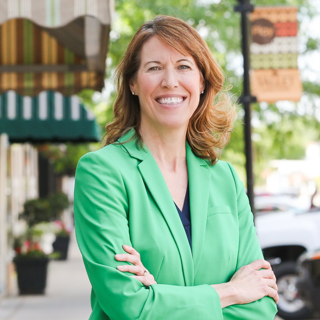 A woman in a green jacket is smiling with her arms crossed.