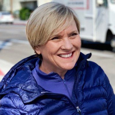 A woman wearing a blue jacket and a purple shirt is smiling.