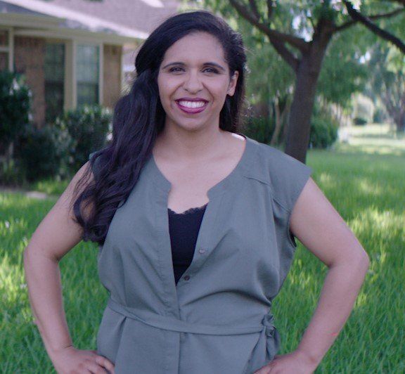 A woman in a green dress is standing in the grass with her hands on her hips.