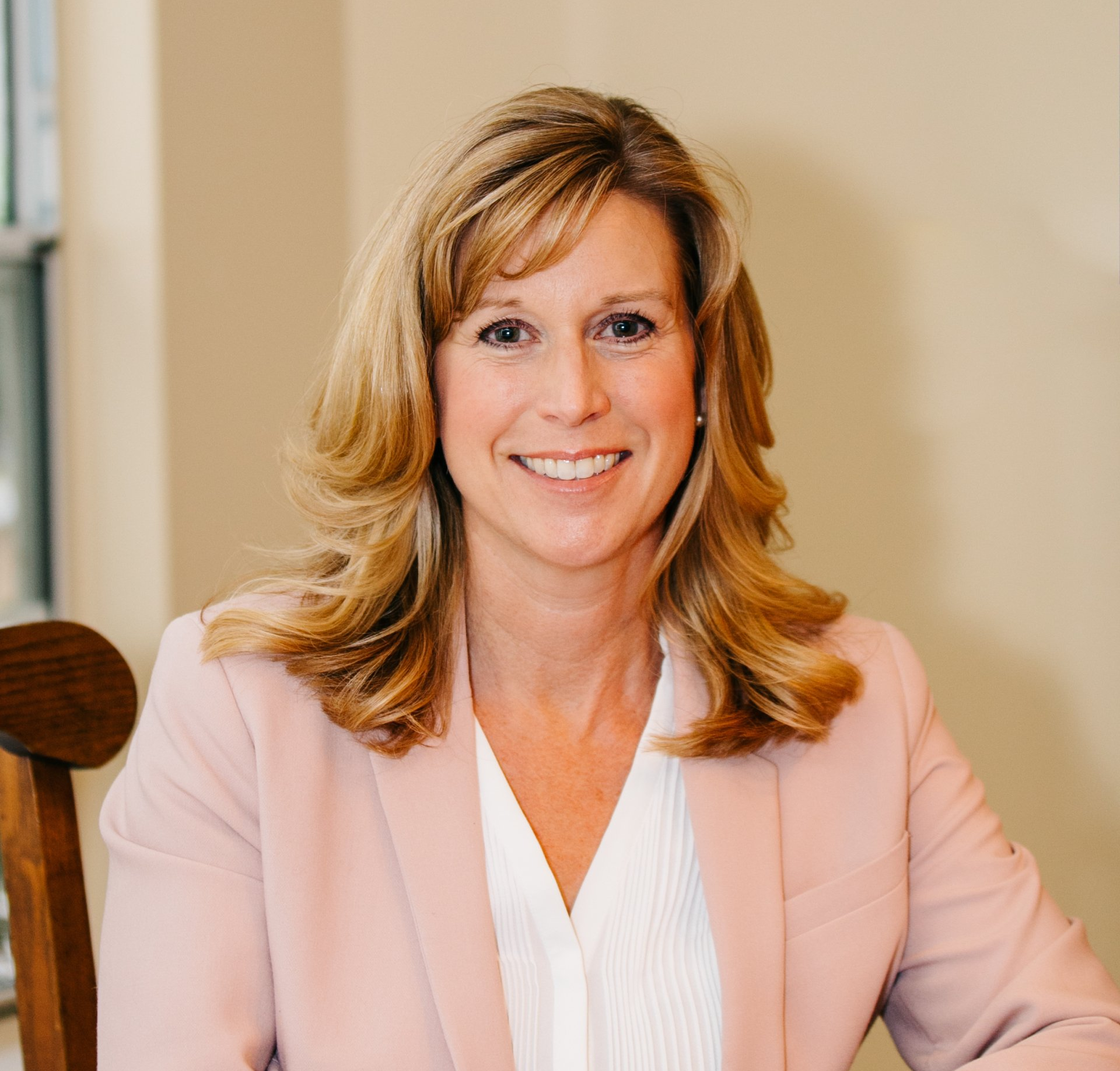 A woman in a pink jacket is sitting in a chair and smiling.