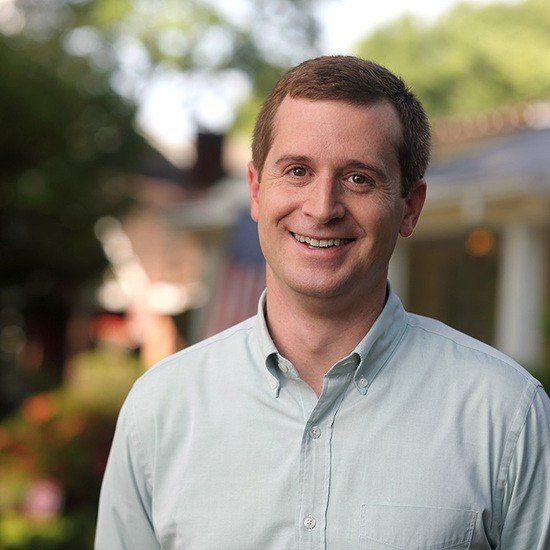 A man in a light blue shirt is smiling for the camera
