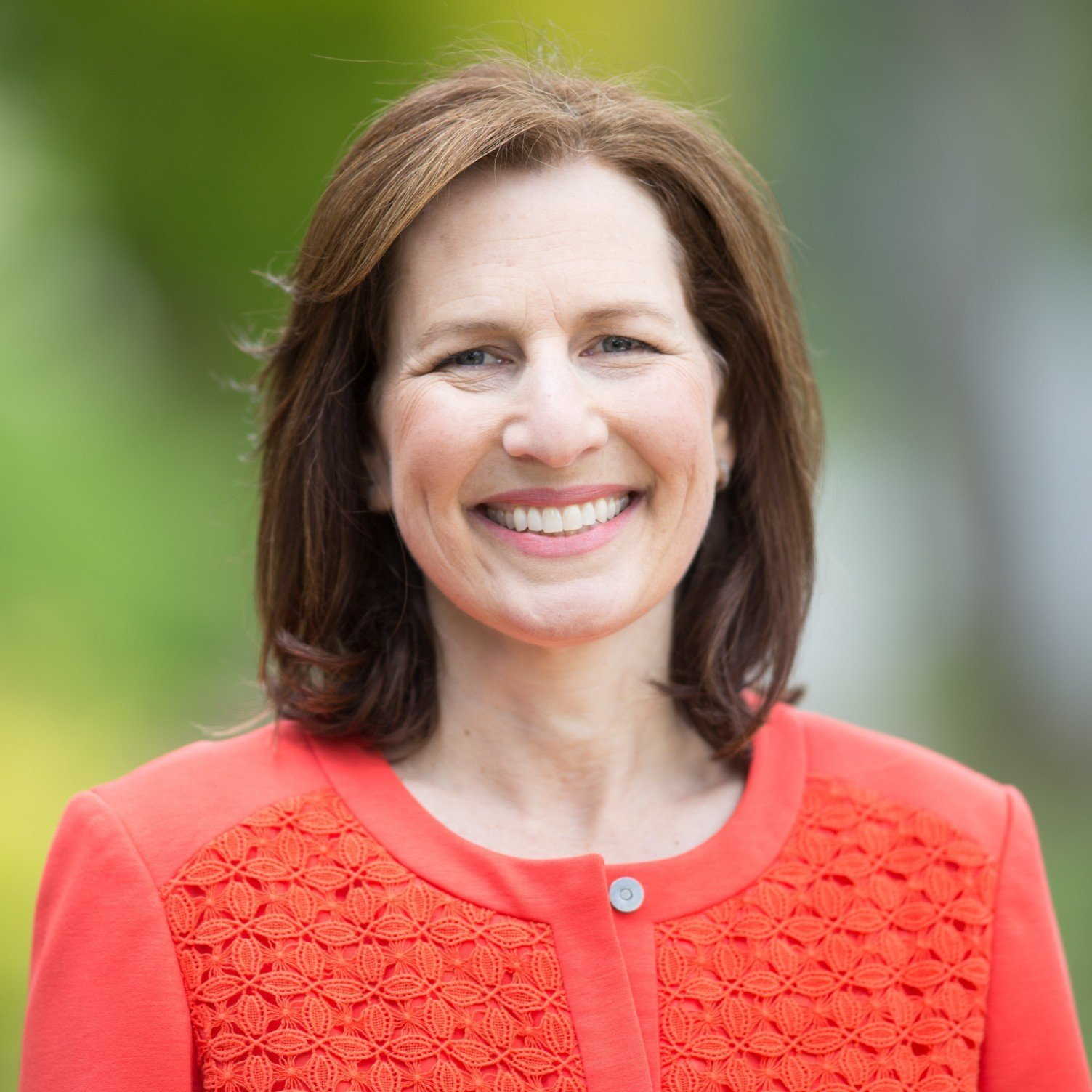 A woman in a red jacket is smiling for the camera.