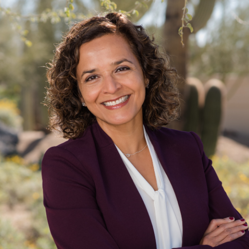 A woman in a purple jacket and white shirt is smiling with her arms crossed.