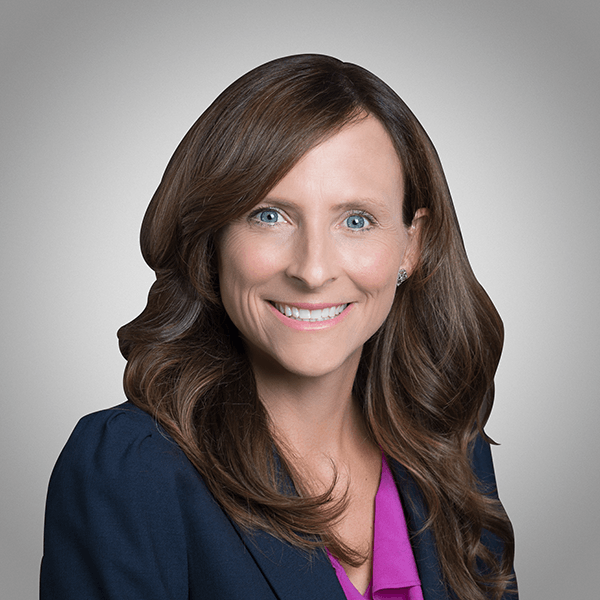 A woman wearing a blue jacket and a purple shirt is smiling for the camera.