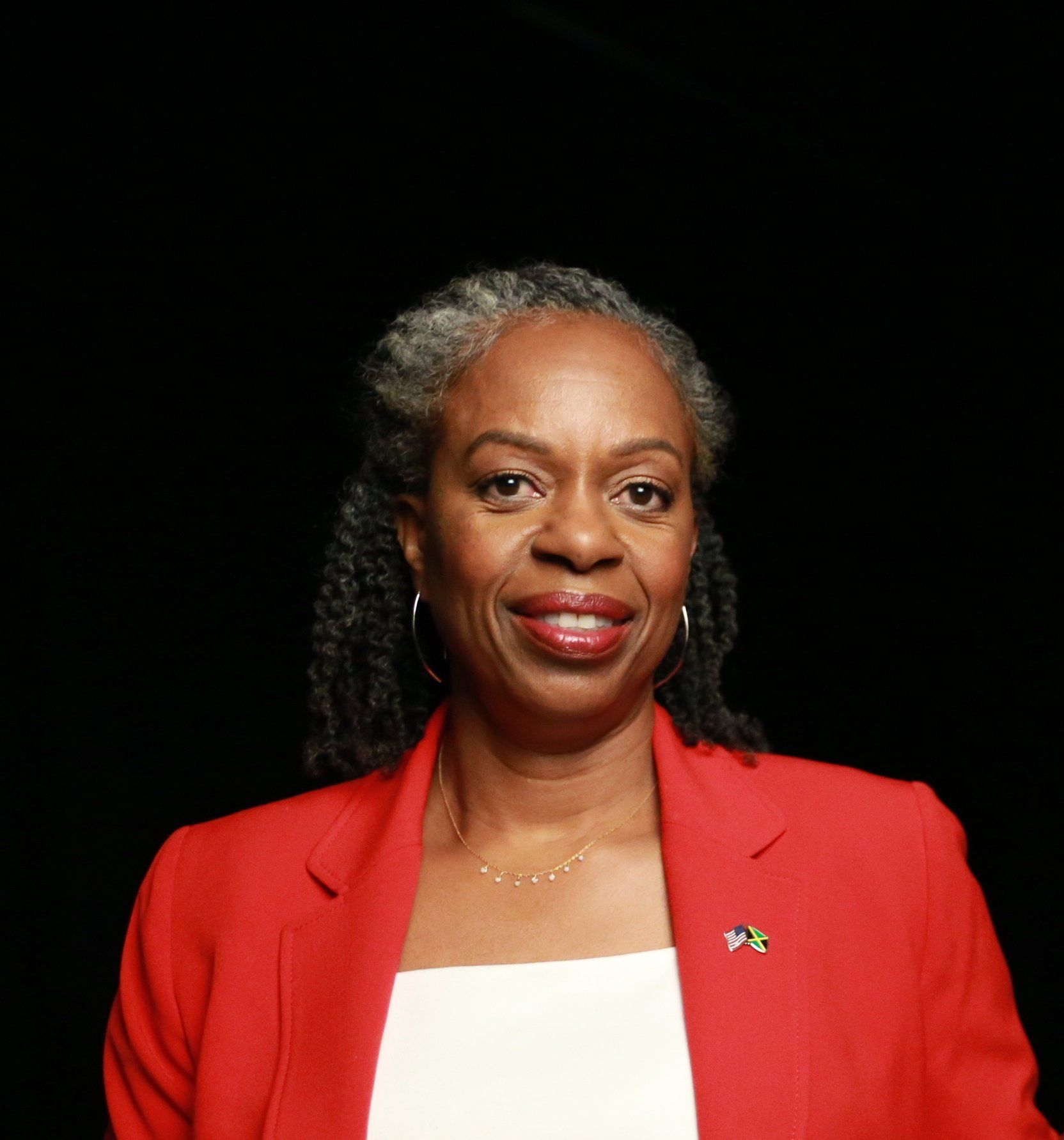 A woman in a red jacket and white shirt is smiling for the camera.