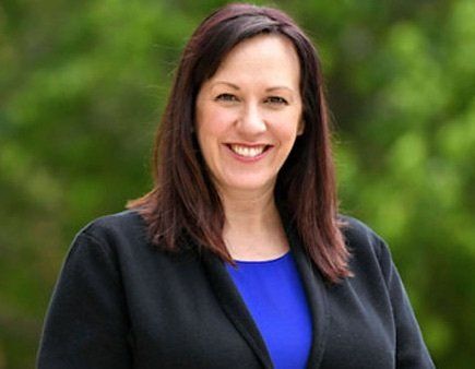 A woman in a blue shirt and black jacket is smiling for the camera.