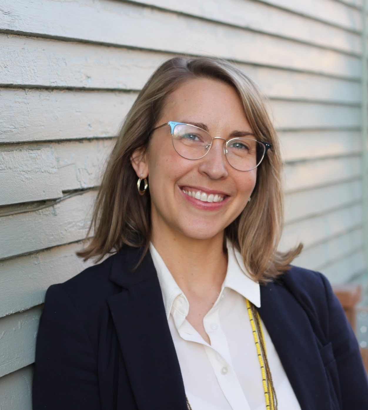 A woman wearing glasses and a jacket is smiling for the camera
