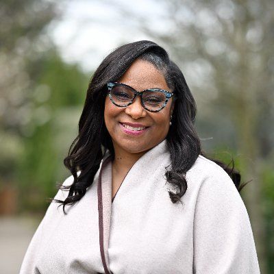 A woman wearing glasses and a white coat is smiling for the camera.