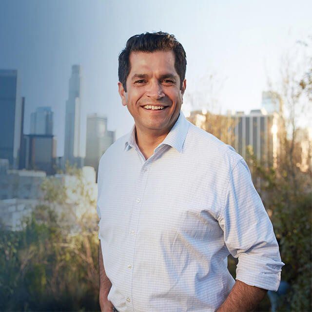 A man in a white shirt is smiling in front of a city skyline