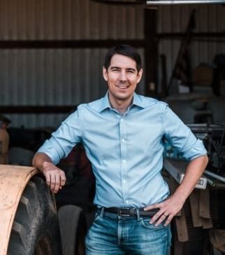 A man in a blue shirt and jeans is leaning on a tractor tire.