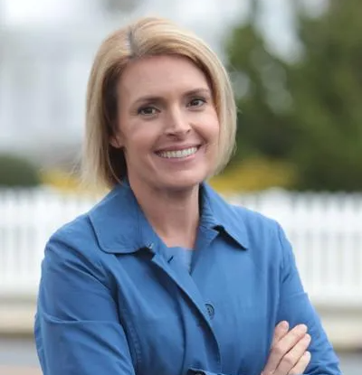 A woman in a blue shirt is smiling with her arms crossed.