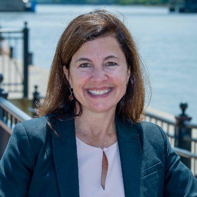 A woman in a blue jacket and pink shirt is smiling for the camera.
