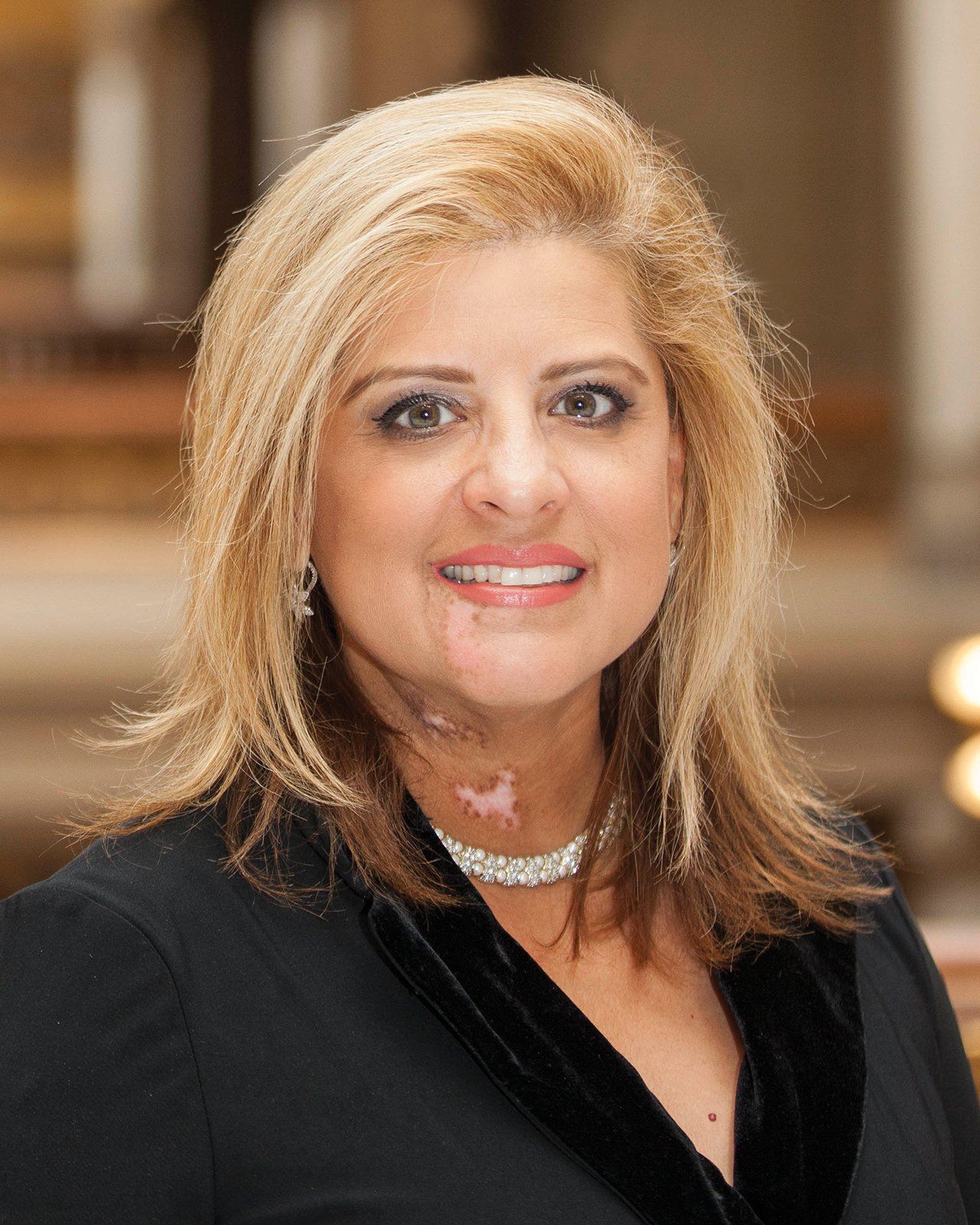 A woman wearing a black jacket and a necklace is smiling for the camera.