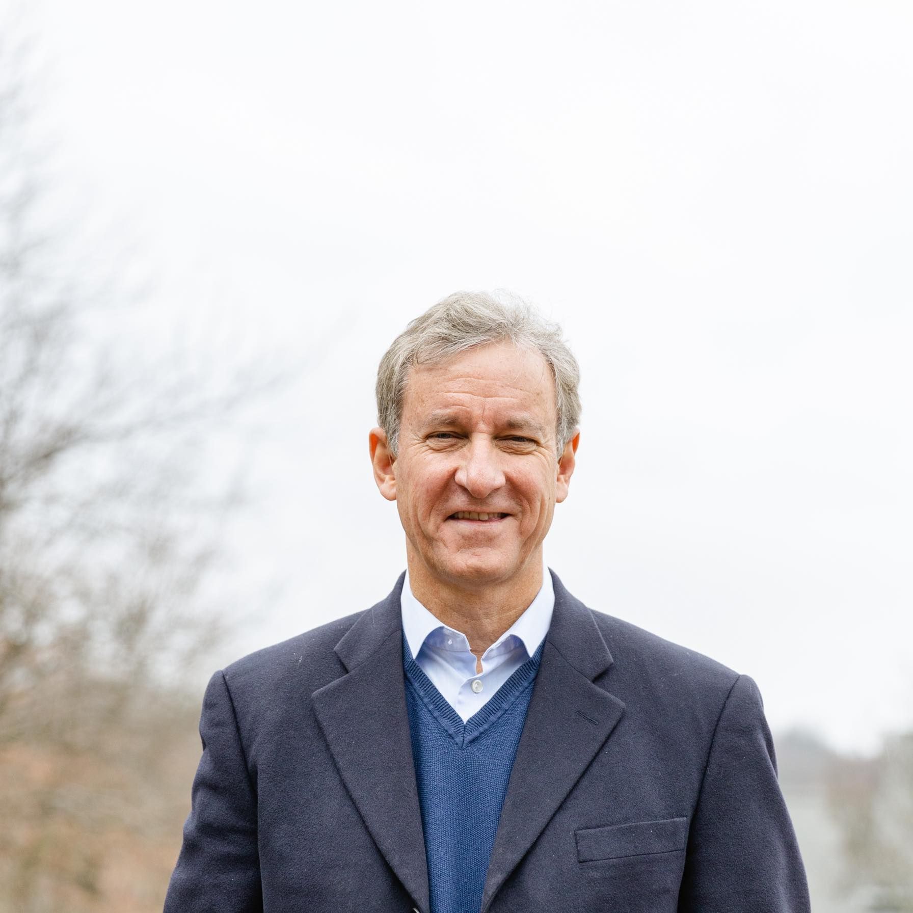 A man in a suit and sweater is smiling for the camera.