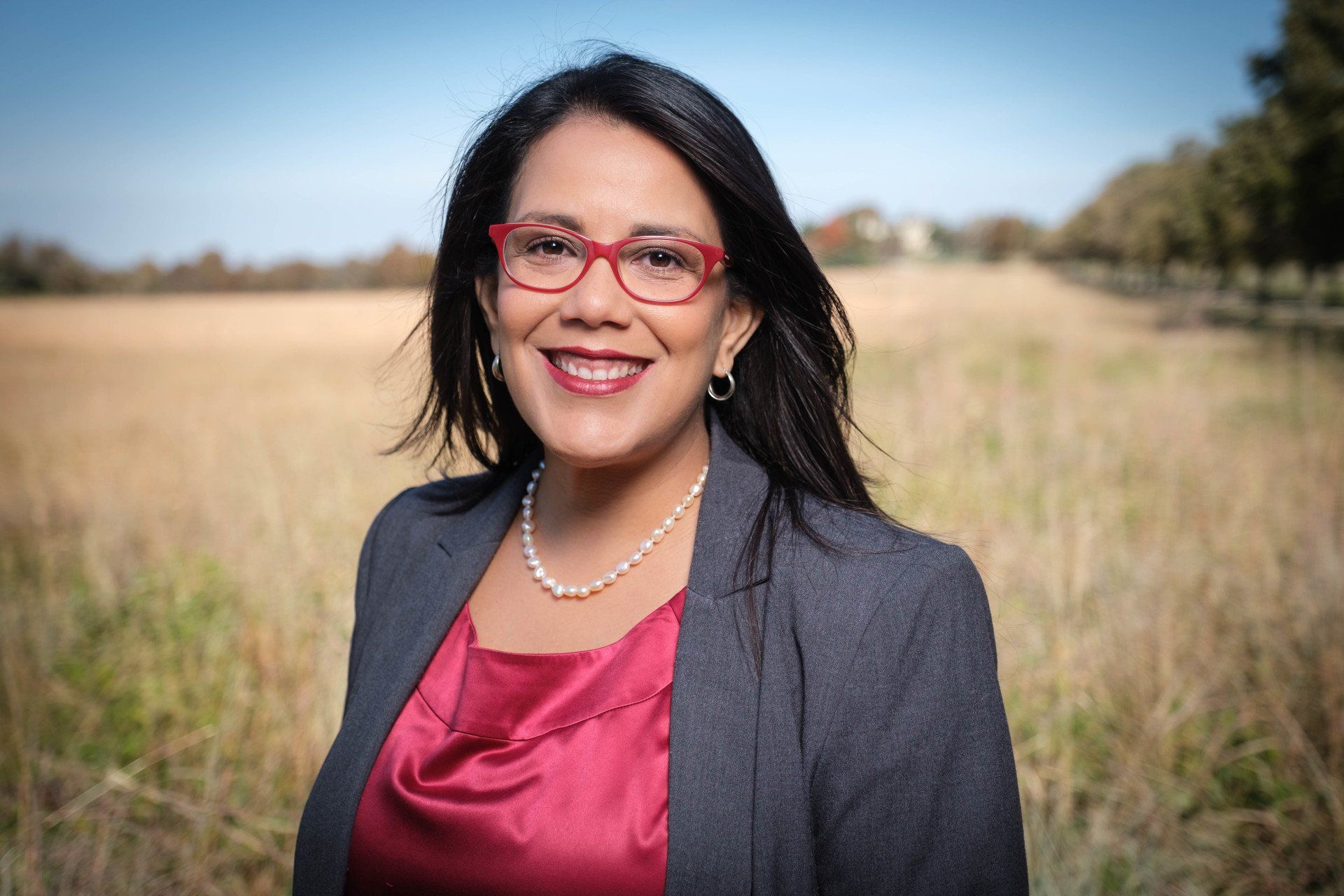 A woman wearing glasses and a red shirt is standing in a field.