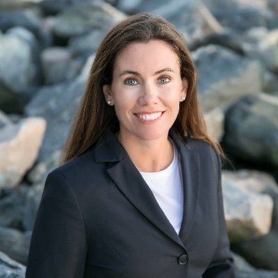 A woman in a suit is standing in front of a pile of rocks and smiling.