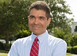 A man in a blue shirt and red tie is smiling for the camera.