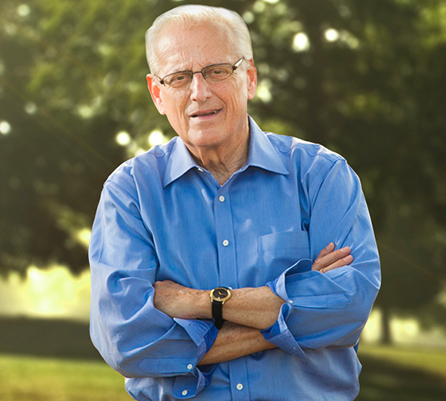 A man wearing glasses and a blue shirt is standing with his arms crossed