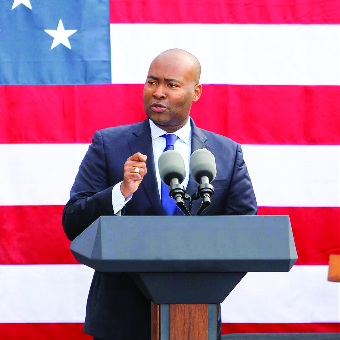 A man in a suit and tie is giving a speech at a podium in front of an american flag