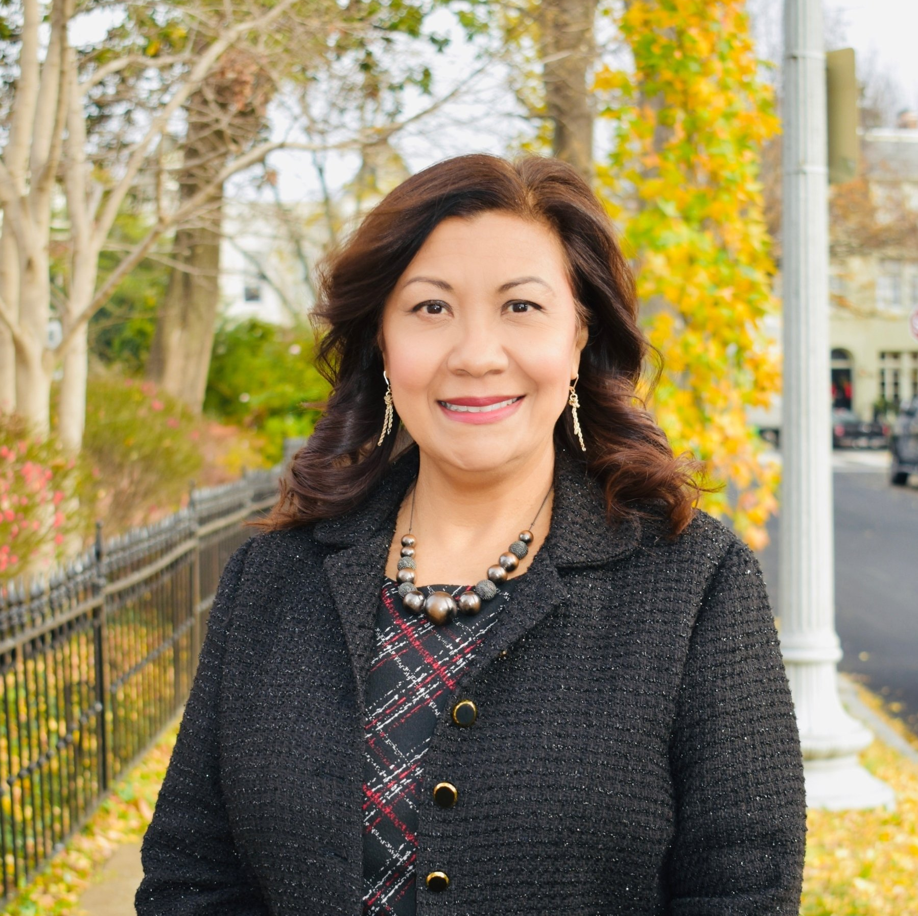 A woman in a black jacket and plaid dress is smiling for the camera.