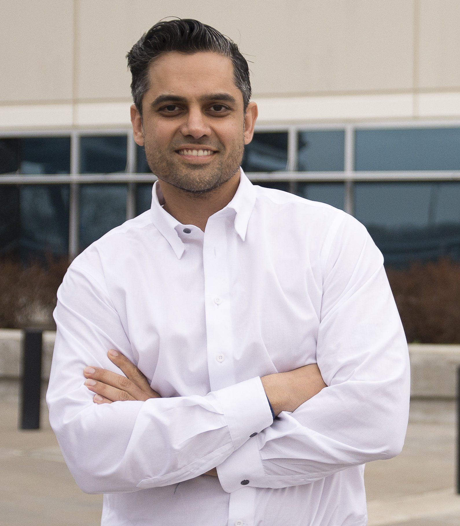 A man in a white shirt is standing with his arms crossed in front of a building.
