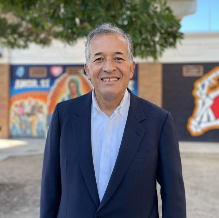 A man in a suit stands in front of a building with a mural on it