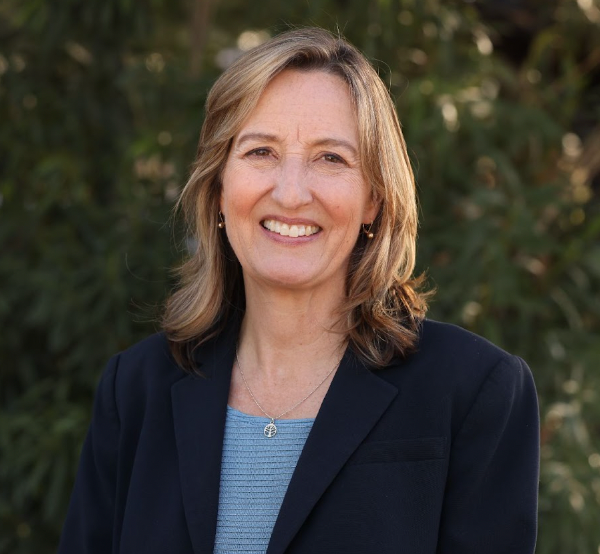 A woman wearing a blue shirt and a black jacket is smiling for the camera.