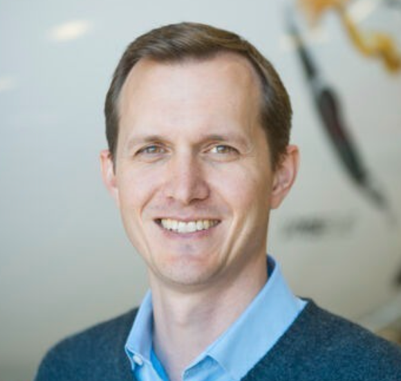 A man in a blue shirt and sweater smiles for the camera