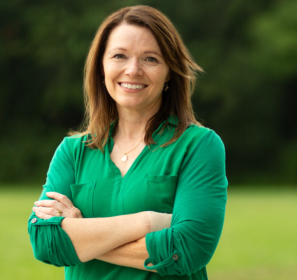 A woman in a green shirt is smiling with her arms crossed
